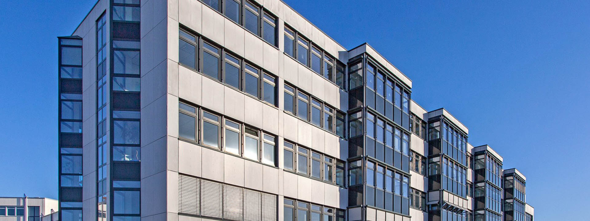 Au&szlig;enansicht eines modernen B&uuml;rogeb&auml;udes mit gro&szlig;en Glasfl&auml;chen und klarer Linienf&uuml;hrung bei sonnigem Himmel