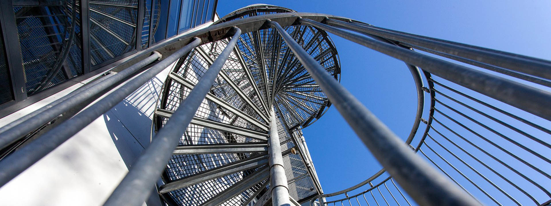 Aufw&auml;rts gerichtete Perspektive auf eine moderne Wendeltreppe aus Metall vor blauem Himmel