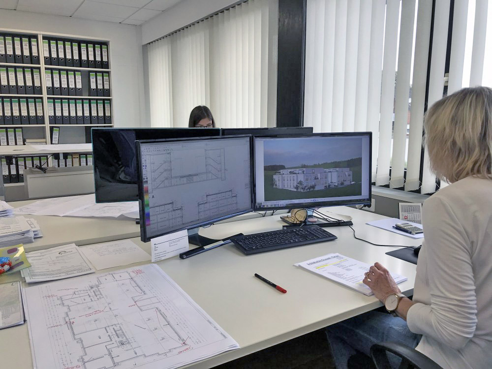 Arbeitsplatz mit CAD-Planung und Visualisierung Zwei Bildschirme mit Bauzeichnung und 3D-Visualisierung, Architektin am Arbeitsplatz mit Plänen und Dokumenten